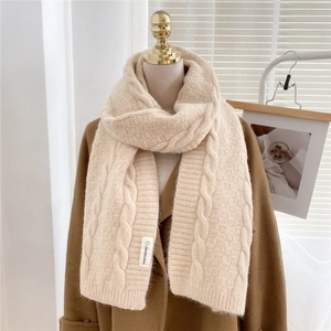 Close-up of beige chunky knit scarf showing 3D cable pattern and premium woven label