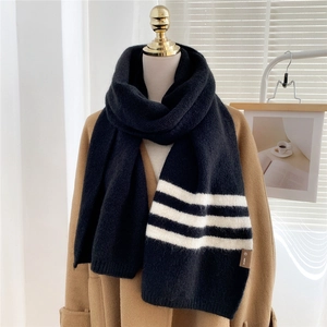 Thick black knit winter scarf with white stripes and leather logo on a beige coat