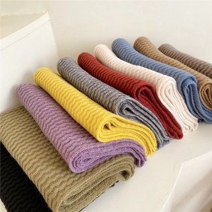 Thick ribbed knit scarf for winter in multiple colors stacked on minimalist white steps