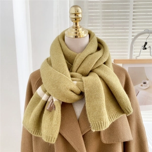 Detail of mustard yellow striped knit scarf with leather patch on camel wool coat