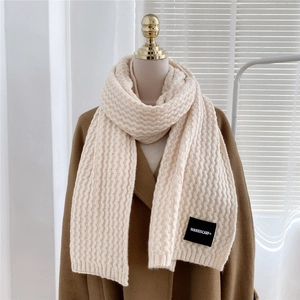 Detail of cream knit scarf with wavy texture and a woven label on thick wool fabric