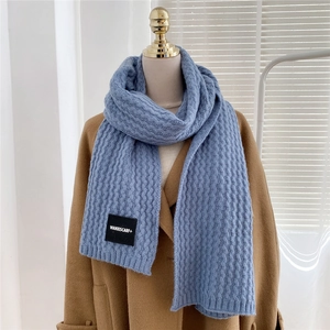 Detailed blue knit scarf with wavy texture and premium fabric brand tag on wool coat