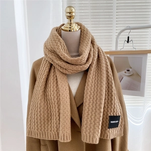 Detail of chunky knit scarf in camel with woven brand tag on textured wool fabric