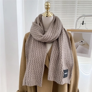 Detailed close-up of brown chunky knit scarf texture with a minimal woven label detail