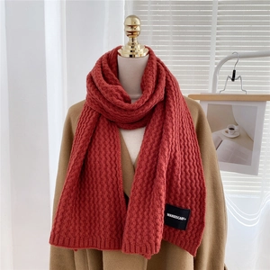 Detailed view of red knitted scarf with wavy texture and black brand woven label