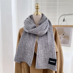 Detail of grey knitted winter scarf with chunky cable knit texture and logo label