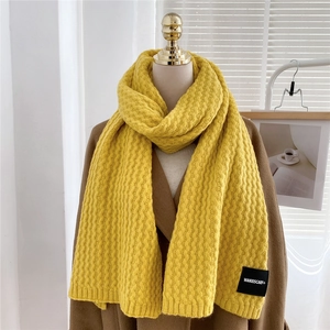 Macro detail of ginger yellow chunky knit scarf featuring wave pattern and brand label