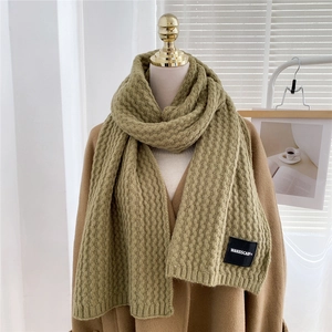 Macro detail of sage green knit scarf featuring wavy texture and branded woven label