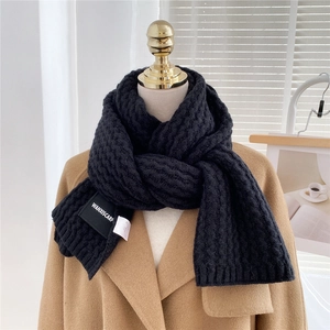 Detail of black thick knitted scarf showing wave texture and woven brand label on camel coat