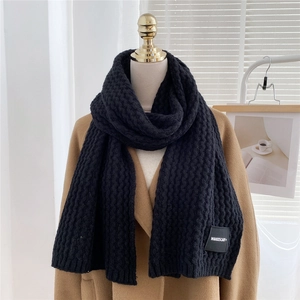 Close-up of black waffle-knit scarf with woven logo label on wool coat display