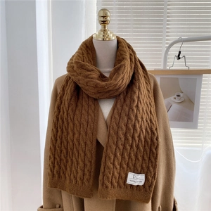Detail view of caramel thick cable knit scarf texture with a white branded fabric label