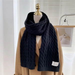 Close-up of thick black knit scarf with cable texture and brand tag on a camel coat