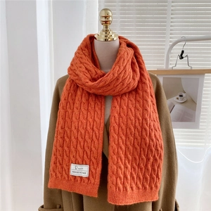 Close-up of orange cable knit scarf texture with a white woven label on heavy fabric