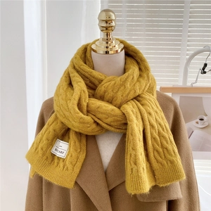 Close-up of yellow chunky knit scarf with vintage cable pattern and branded fabric label