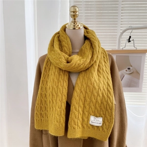 Detailed close-up of bright yellow cable knit scarf with decorative woven brand label