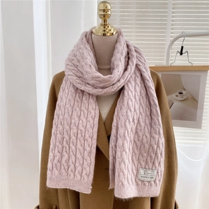 Close-up of pink knitted scarf showing chunky cable knit texture and woven brand label