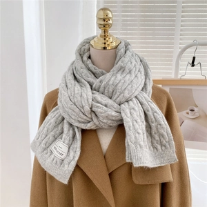 Detail of light gray cable knit winter scarf with a white woven label on camel wool coat