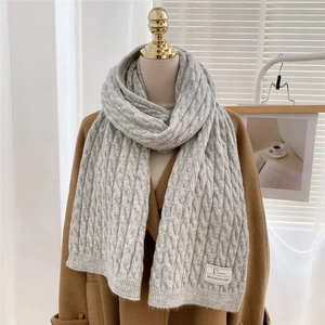 Detail of grey cable-knit winter scarf with fabric brand label on a wool coat