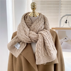 Close-up of beige cable knit scarf texture showing thick weave and fabric brand label