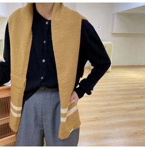 Detail of a ginger yellow knitted scarf with white stripes worn over a black cardigan