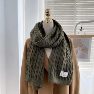 Close-up of olive green cable knit scarf featuring a white woven brand label detail