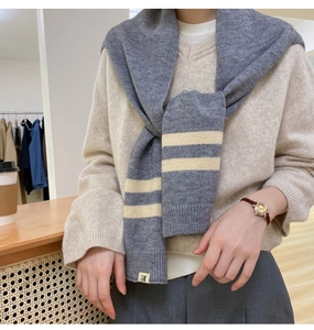 Detail of grey striped knitted shawl with 'H' label styled over a beige sweater