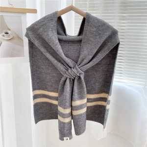 Detail of grey knitted shawl with beige stripes hanging on a wooden hanger