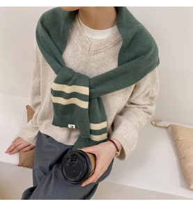 Detail shot of green and beige striped knit shawl scarf with minimalist woven brand tag