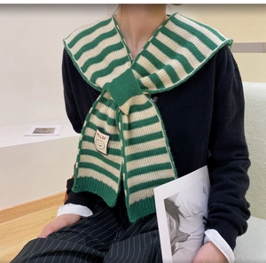 Detail of green and white striped knit shawl featuring a smile logo patch and button