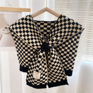 Close-up of black and white checkerboard knit shawl with a cartoon smiley face patch