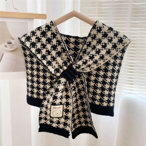 Detail of houndstooth knit shawl featuring a black ribbed hem and branded smiley face patch
