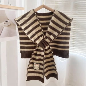 Close-up of knit striped shawl with embroidery patch on soft neutral background