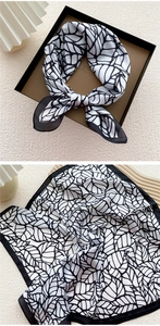 Detail of a black and white silk scarf with leaf pattern and elegant gift box packaging