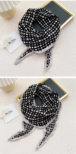 Detail of black and white checkered knit scarf with gray wave stitched edges on a textured surface
