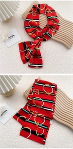 Detail of red silk scarf with belt buckle patterns and stripes on a wooden tray
