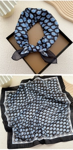 Detail of a square scarf with blue paisley print on black fabric in a gift box