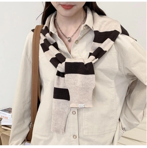 Détail d'un châle en tricot rayé drapé sur une chemise utilitaire beige à boutons
