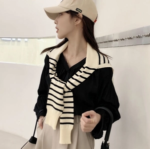 Detail of striped knitted shawl draped over black shirt and khaki trousers with cap