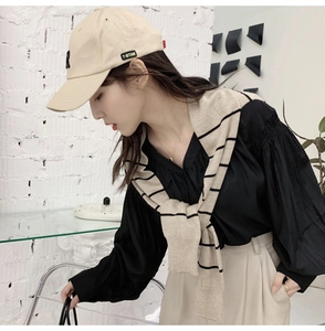 Detail of a beige baseball cap with T-STAR label paired with a striped knit shawl