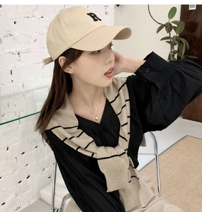 Close-up of a beige knitted striped shawl styled over a black shirt with a baseball cap