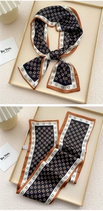 Detail of printed silk scarf with monogram pattern and contrast border on gold tray