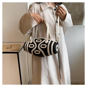 Detail of a cylindrical two-tone leather handbag with abstract geometric lines and gold hardware