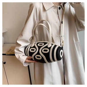 Detail of a black and white cylinder bucket bag with oval geometric pattern and crossbody strap