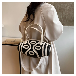 Close-up of black leather cylinder bag with white abstract lines and wide shoulder strap