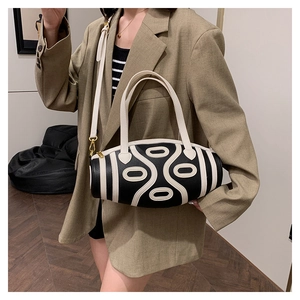 Detail of cylindrical contrast bag with cream geometric patterns and gold-tone hardware