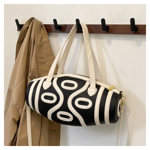 Detail view of monochrome cylindrical crossbody bag hanging with adjustable strap and handles