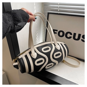 Detail of a black and white cylinder bag with top handles and gold hardware zipper