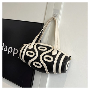 Detail of a retro black and cream cylinder bag with fine faux leather and golden hardware