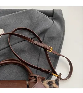 Detail of adjustable leather strap with gold buckle on leopard print shoulder bag