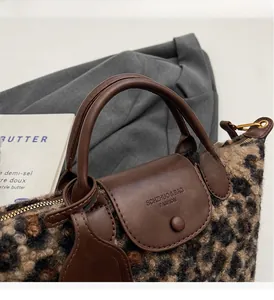 Close-up of leopard print plush handbag showing brown leather handle and metal zipper detail